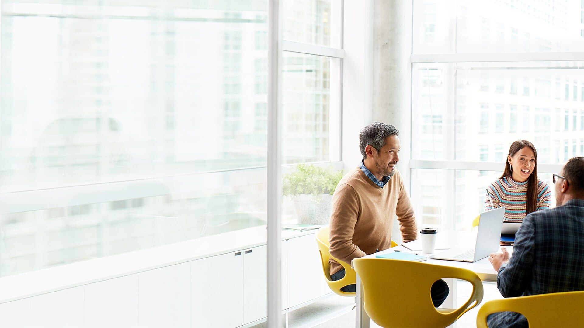 In a brightly lighted boardroom in a modern office building, three colleagues are involved in a lively discussion.