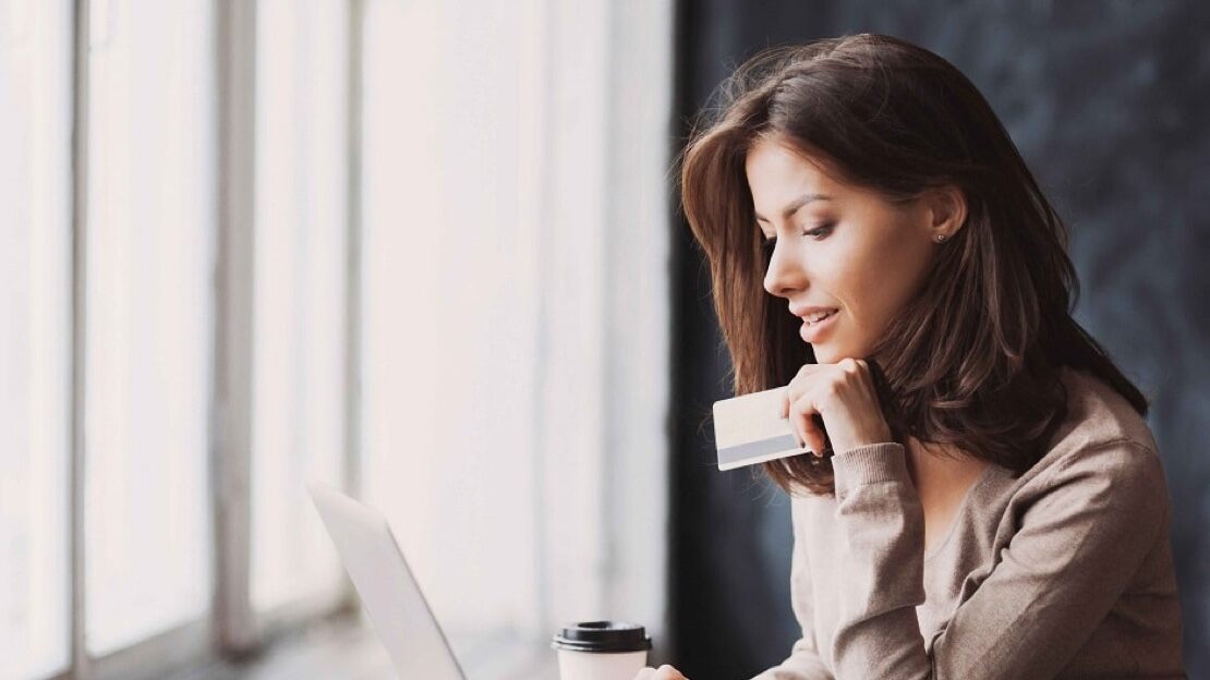 An attractive young woman holds her credit card while looking at her laptop screen