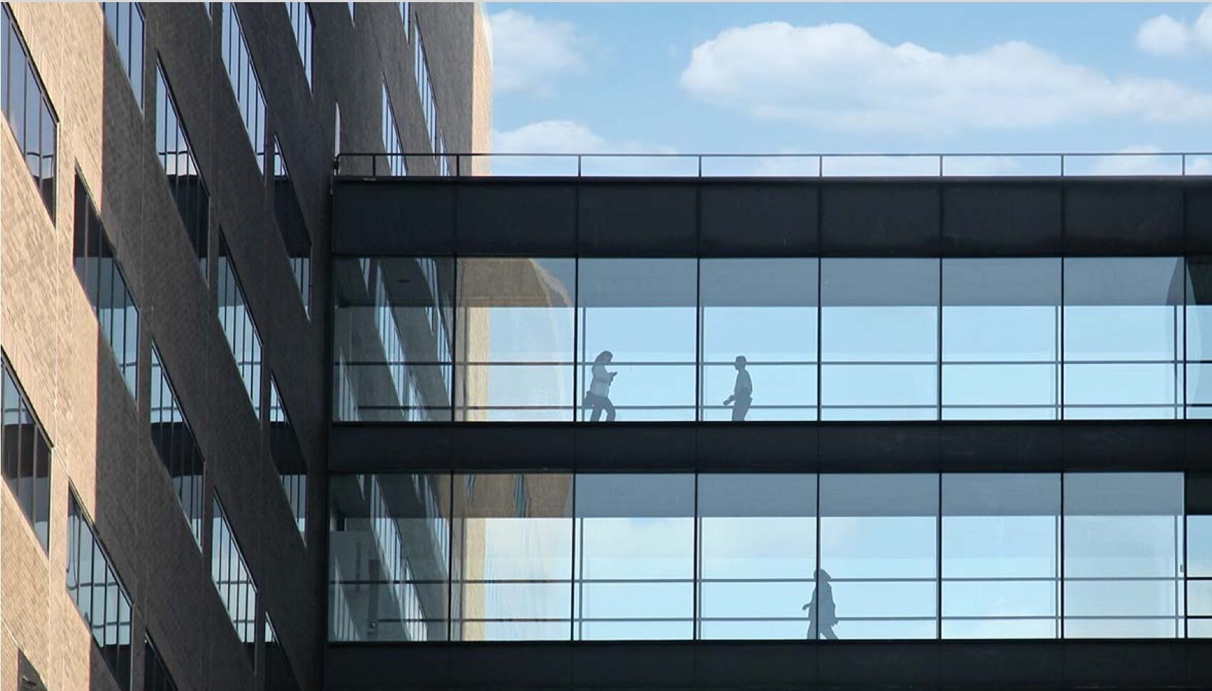 People are in a glass walkway between two modern building