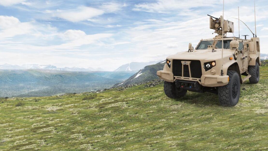 A Oshkosh built military vehicle is parked on a cliff overlooking a valley