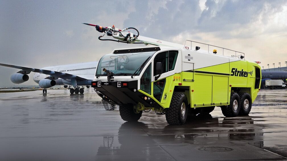 An airport maintenance vehicle is parked in front of a passenger jet on a tarmac