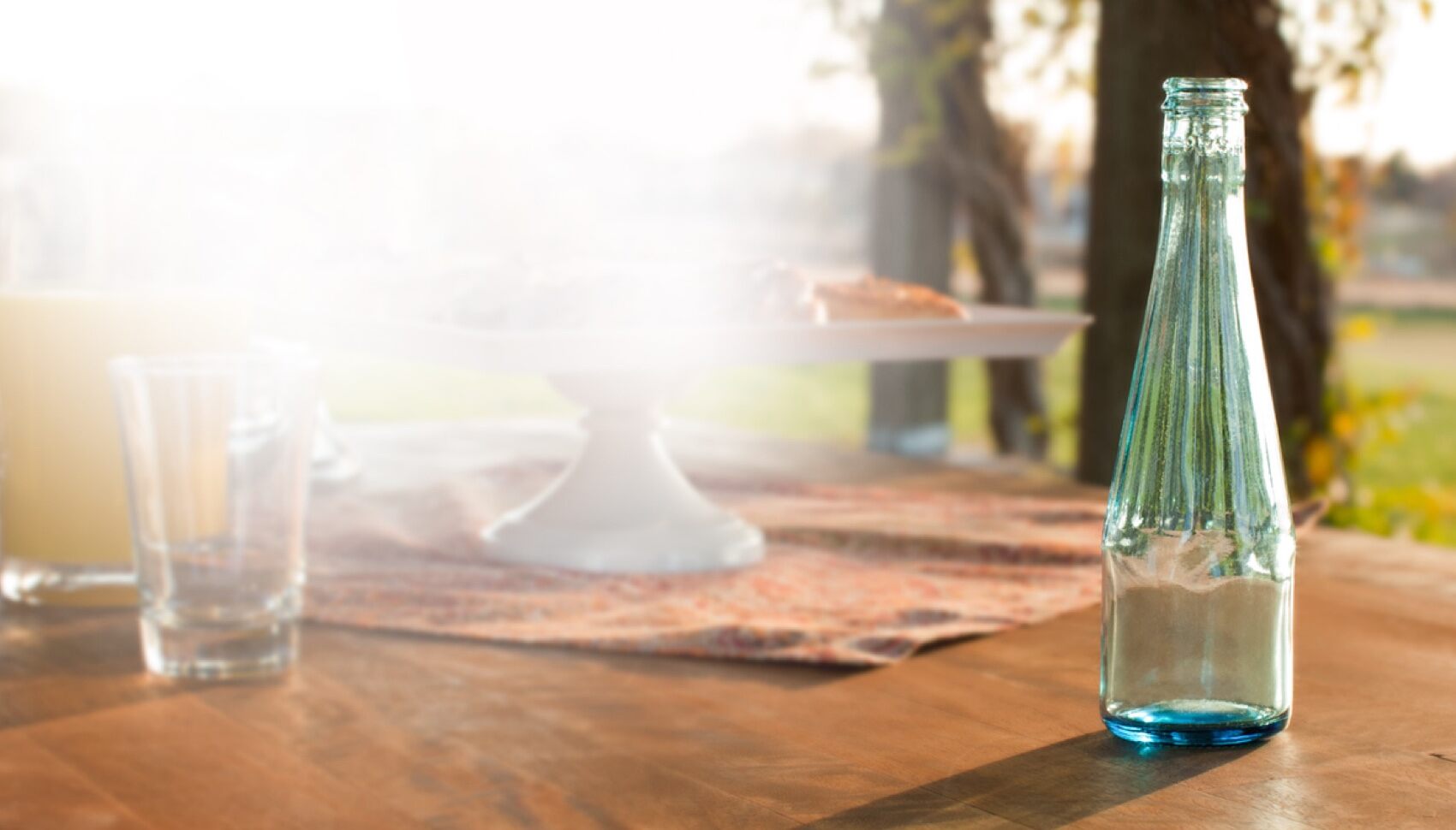 A clear glass bottle sits on a wooden patio table on a sunny day