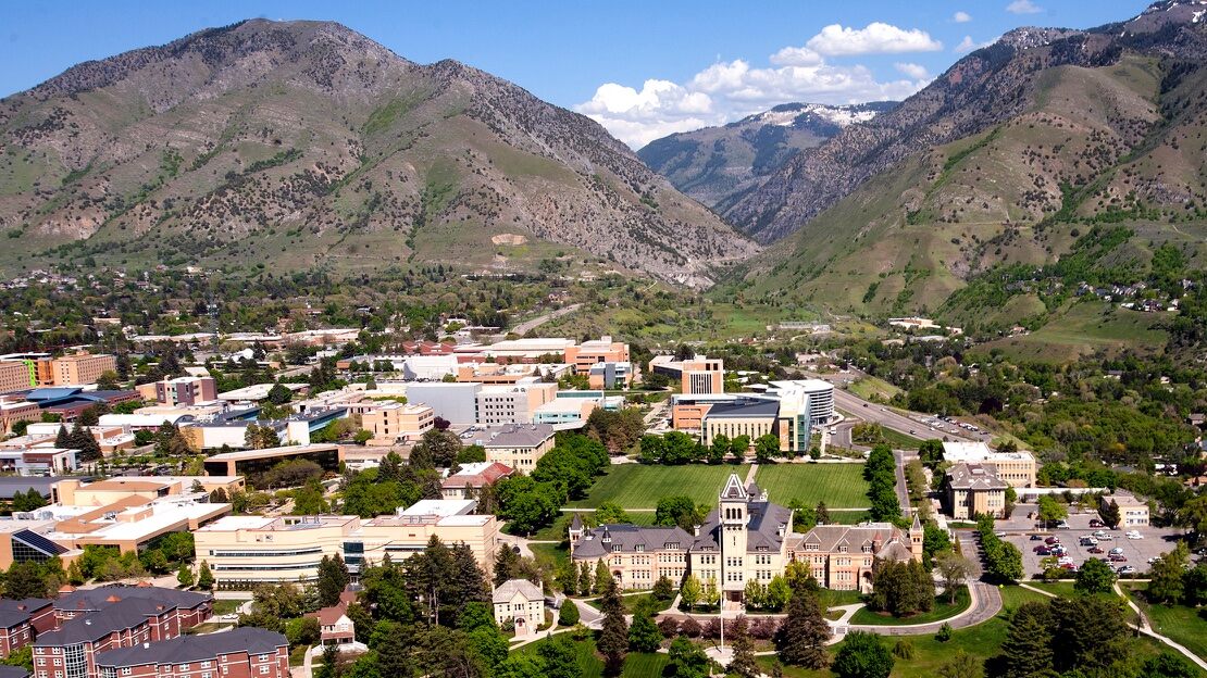 An aerial view of the Utah State University campus nestled between some mountains on a sunny, spring day