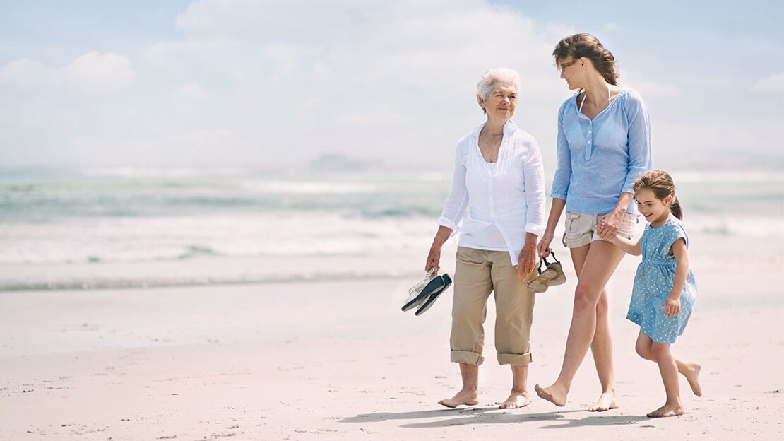 an older woman, a younger woman, and a young girl walk on the beach in the sun
