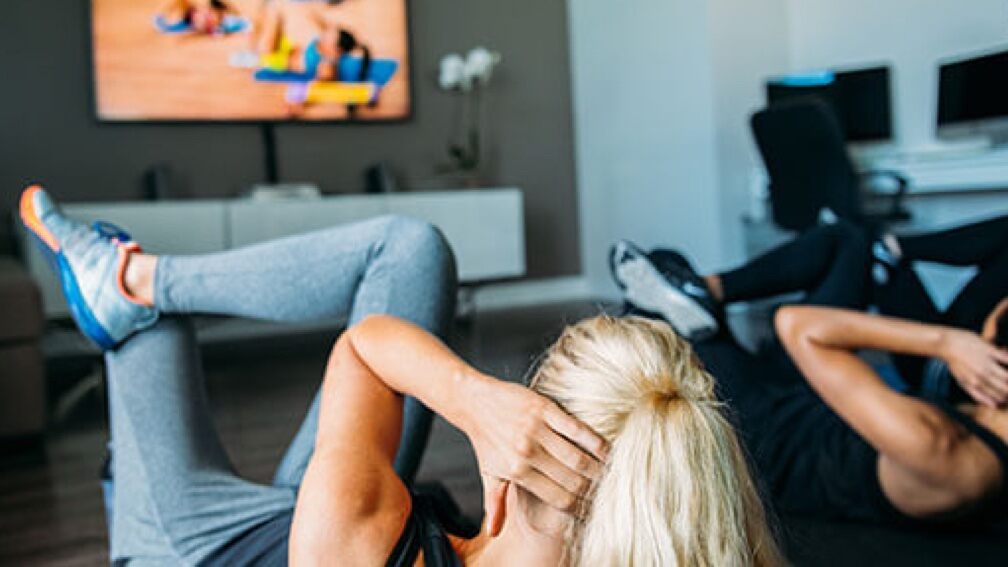 Two Beachbody people are working out to an exercise video on a big screen