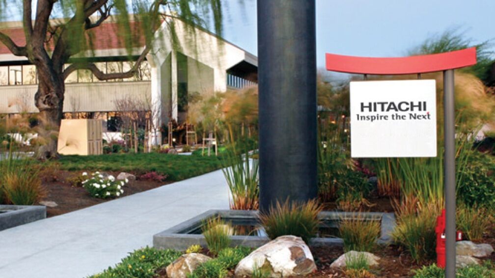 A garden with a view of a Hitachi building with a sign reading, “Hitachi Inspire the Next”